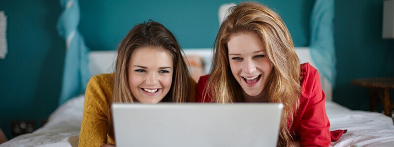 Two girls laughing while looking at a laptop screen.
