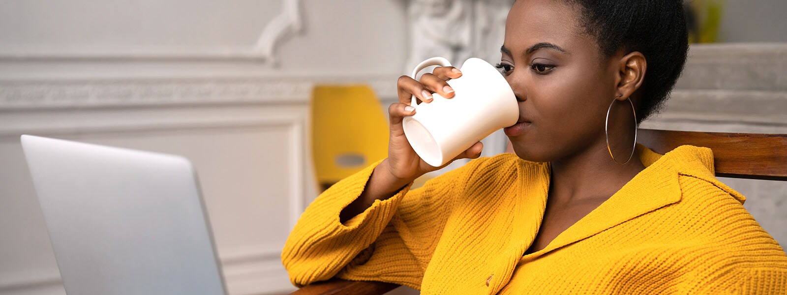 An Black woman researches ways to protect her devices and network from drive-by downloads as she drinks her morning coffee. 