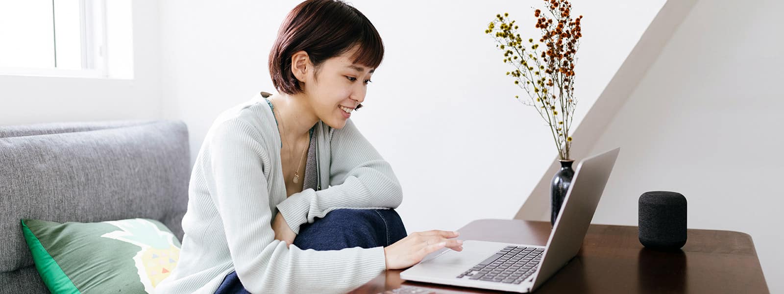 a woman smiles as she sits on a couch and uses her laptop, suggesting that she is glad to be freeing up her computer’s RAM