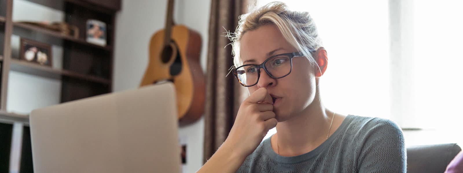 a blonde haired woman with black glasses looks concerningly at her laptop computer, indicating she might be a spear phishing victim