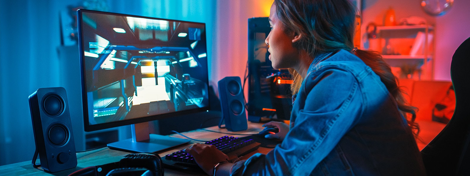 a woman in a jean jacket plays a computer game in a dark room